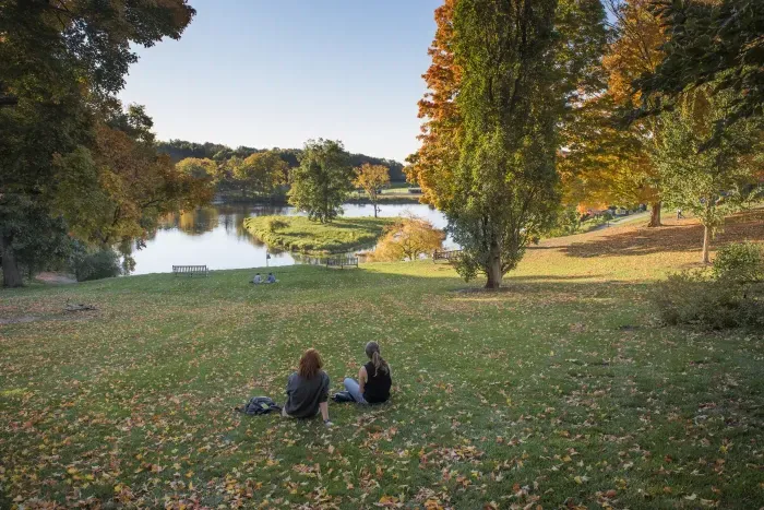 Two students sitting in front of 天堂的池塘 in the fall.